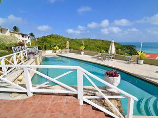 Outdoor pool area with a panoramic view of the coastline and surrounding greenery, equipped with sun loungers and vibrant yellow umbrellas